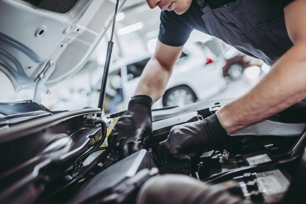 A skilled mechanic in a dark blue uniform performs motor repair on a vehicle in a well-equipped garage, focusing intently as he adjusts components under the open hood.